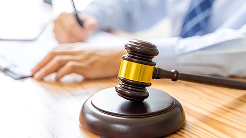 Person writing on paper with gavel on desk